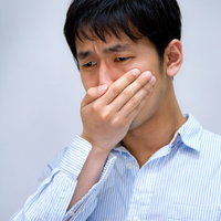 白い背景の前で目頭を押さえて泣きそうな表情の男性の写真