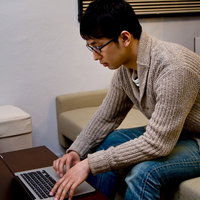 ソファーに座りノートPCを操作するデザイナーの男性の写真