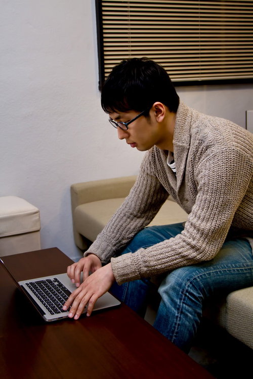 ソファーに座りノートPCを操作するデザイナーの男性