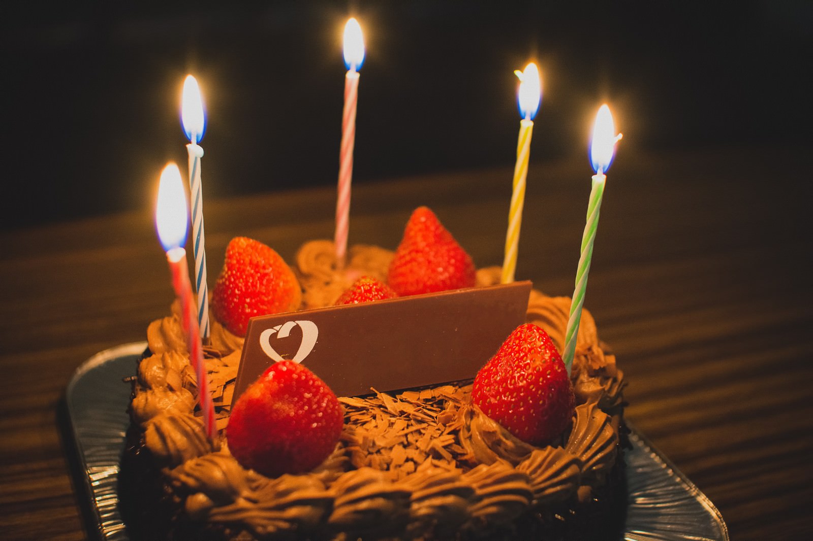 赤いいちごと数本のろうそくが飾られた、チョコレートケーキ