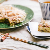 キャベツたっぷりのお好み焼きと緑の皿、箸と日本茶のテーブルコーディネートの写真