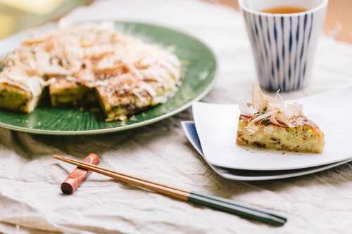 キャベツたっぷりのお好み焼きと緑の皿、箸と日本茶のテーブルコーディネート