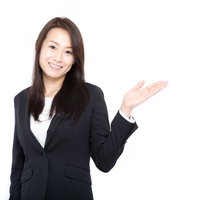 コチラですと案内するスーツ姿の女性が笑顔で右手で指し示しているの写真