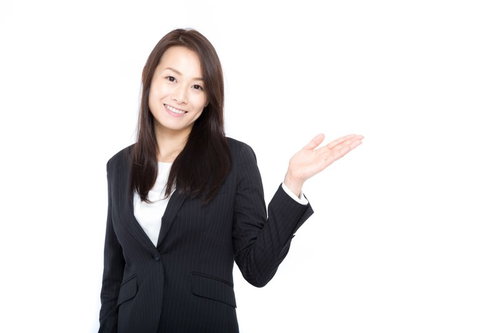 コチラですと案内するスーツ姿の女性が笑顔で右手で指し示している