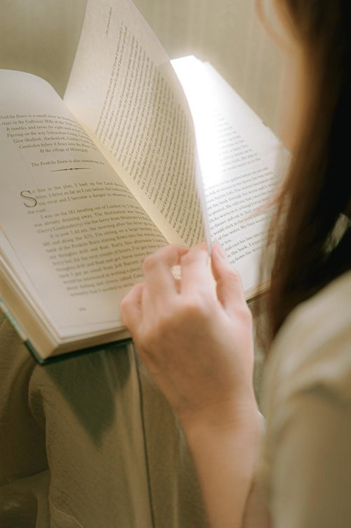 自然光の下で洋書をページめくりする女性の手元