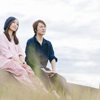 農作業を終えて草土手で休憩するもんぺ姿の若い夫婦の写真