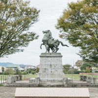 秋の大刀洗公園に立つ菊池武光騎馬像と紅葉の樹々の写真