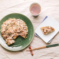 食卓を飾るお好み焼きと桜エビの一品～緑のプレートに盛られた粉もの料理の写真