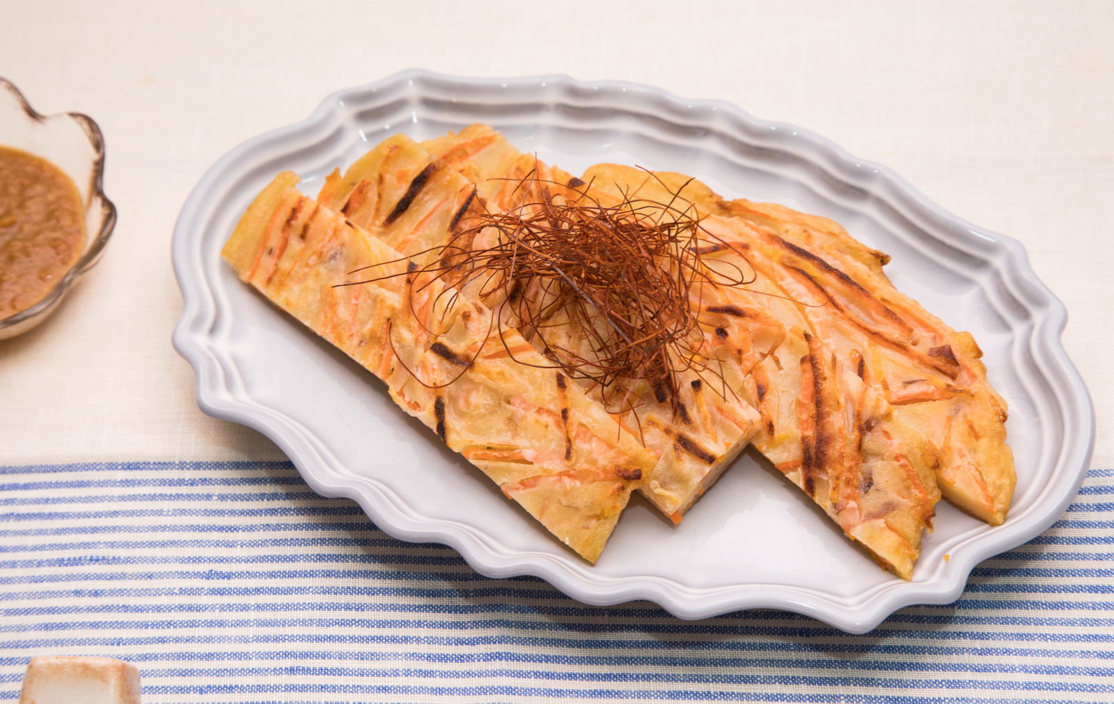 白い皿に盛られたこんがり焼いたにんじんチヂミ。かつお節がのっている
