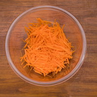 透明なボールに入った人参の千切り、木目調テーブルの上の写真