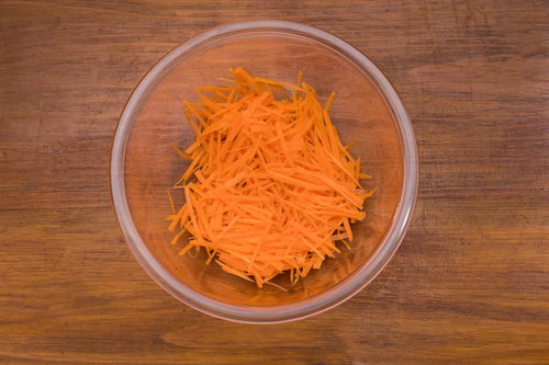 透明なボールに入った人参の千切り、木目調テーブルの上