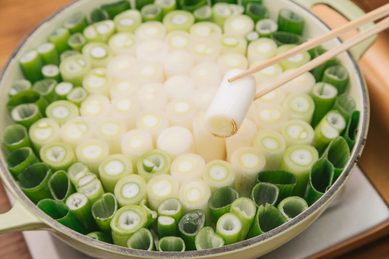 白ねぎの輪切りと豆腐が浮かぶ透き通ったすき鍋に、木製の箸が置かれている