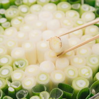 箸でつまむ鍋いっぱいのネギ、白ネギと青ネギの盛り付けの写真