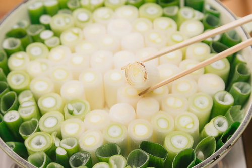 箸でつまむ鍋いっぱいのネギ、白ネギと青ネギの盛り付け