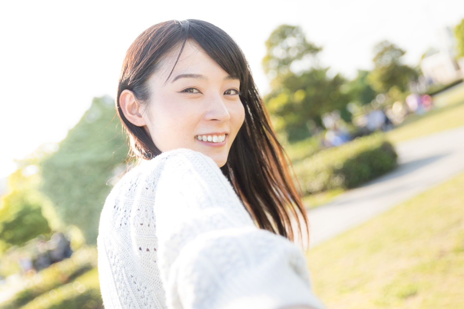 白い服を着て振り返りながら笑顔を見せる女性［モデル：たけべともこ］