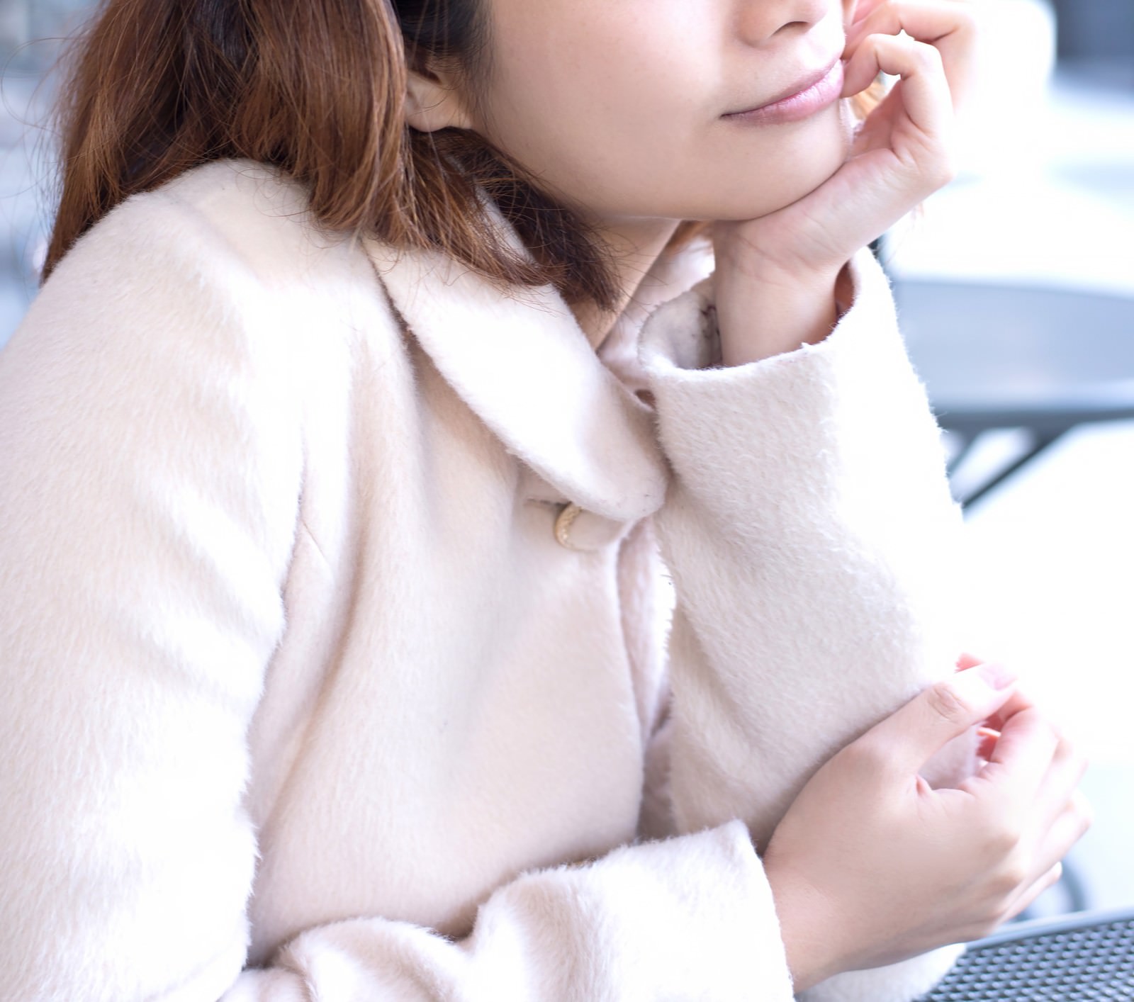 ピンクのコートを着て頬杖をつき考える女性