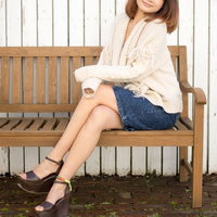 木製ベンチに座るレーストップスとデニムスカートの女性の写真