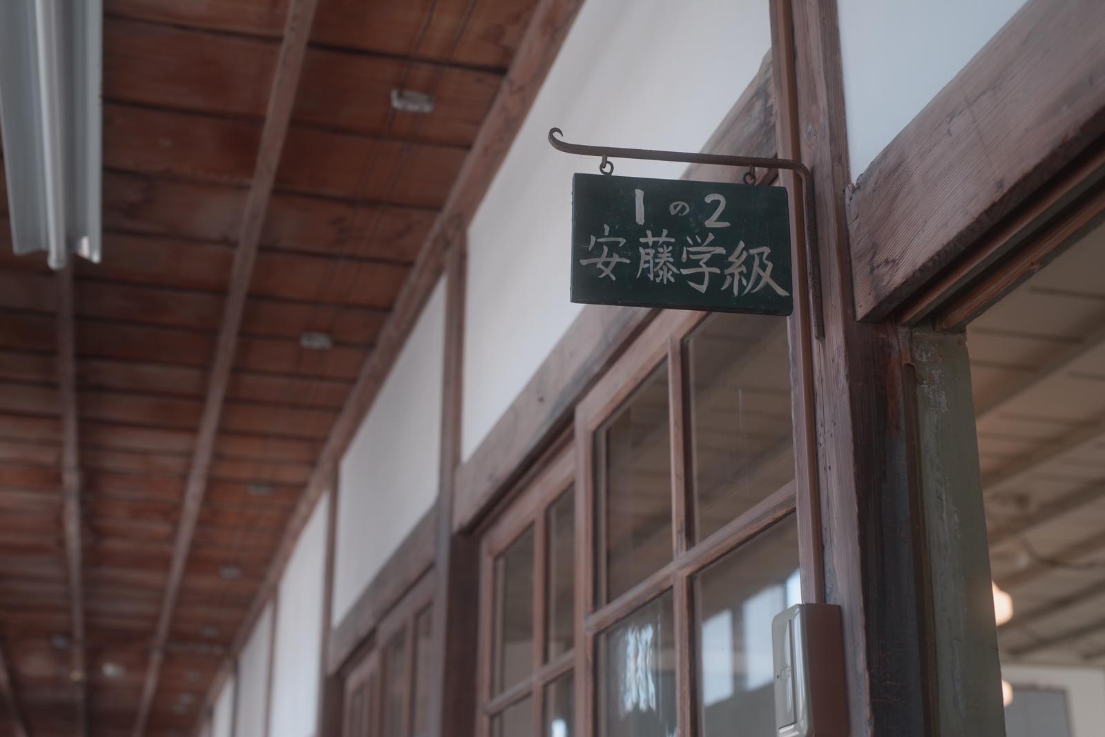 木造校舎の廊下に掲げられた黒い学級表示板に白く書かれた「1の2 安藤学級」