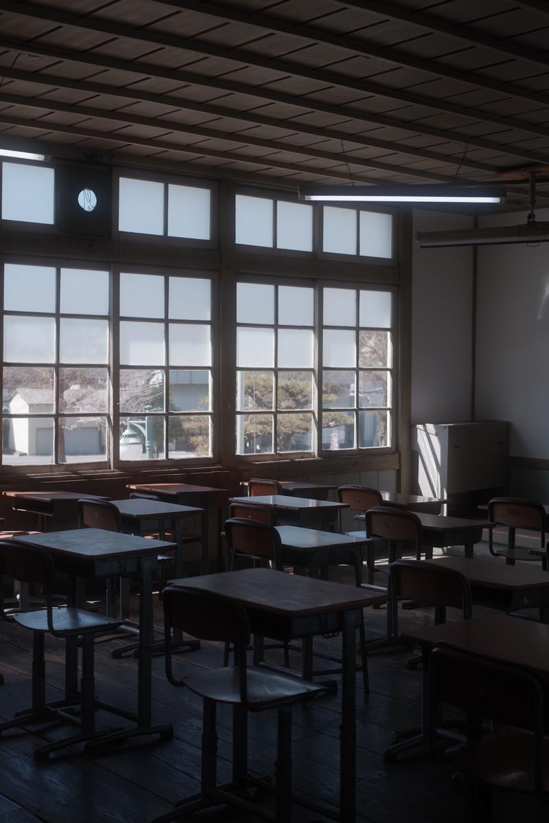 放課後の旧校舎教室に整列する学習机と椅子、格子窓から光が入る