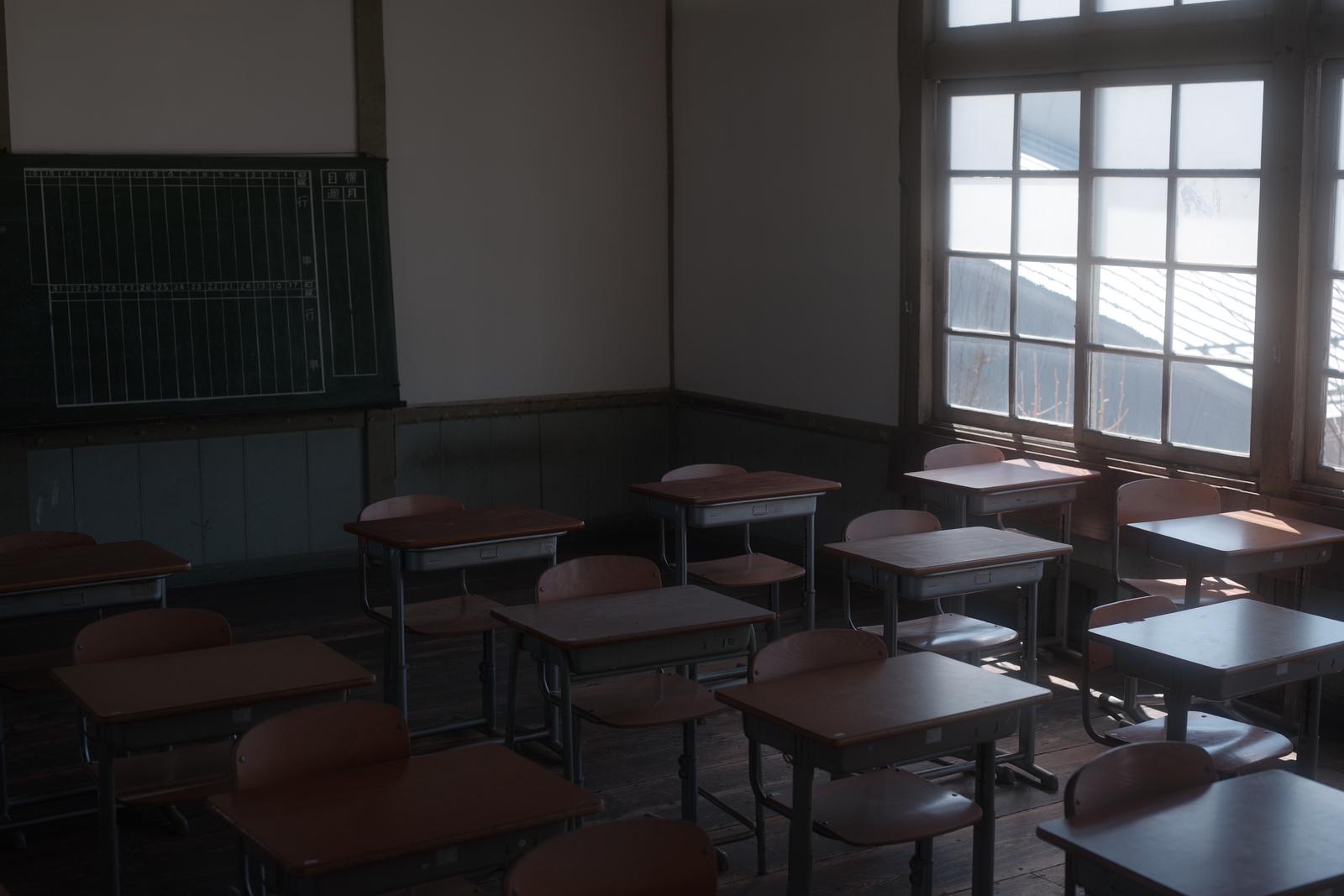 窓からの光が差し込む放課後の教室に並ぶ木製の学習机と椅子