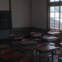 放課後の教室に並ぶ学習机と椅子、窓から差し込む光の写真