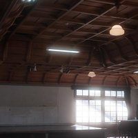 光差す旧遷喬尋常小学校の講堂、木組み梁と照明の写真