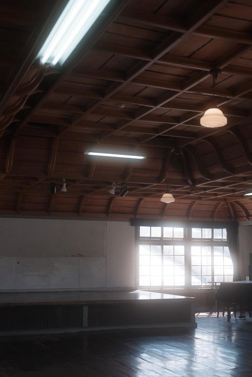 光差す旧遷喬尋常小学校の講堂、木組み梁と照明