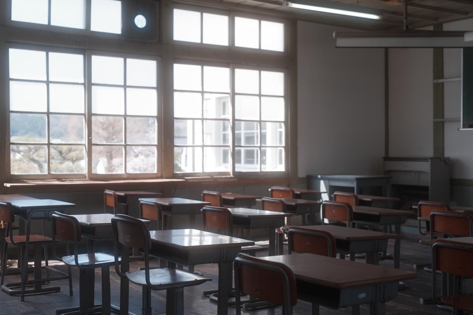 放課後の教室内で、窓辺に整列された学習机と椅子
