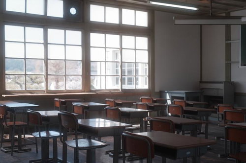 窓辺に整然と並ぶ学習机と椅子、放課後の教室
