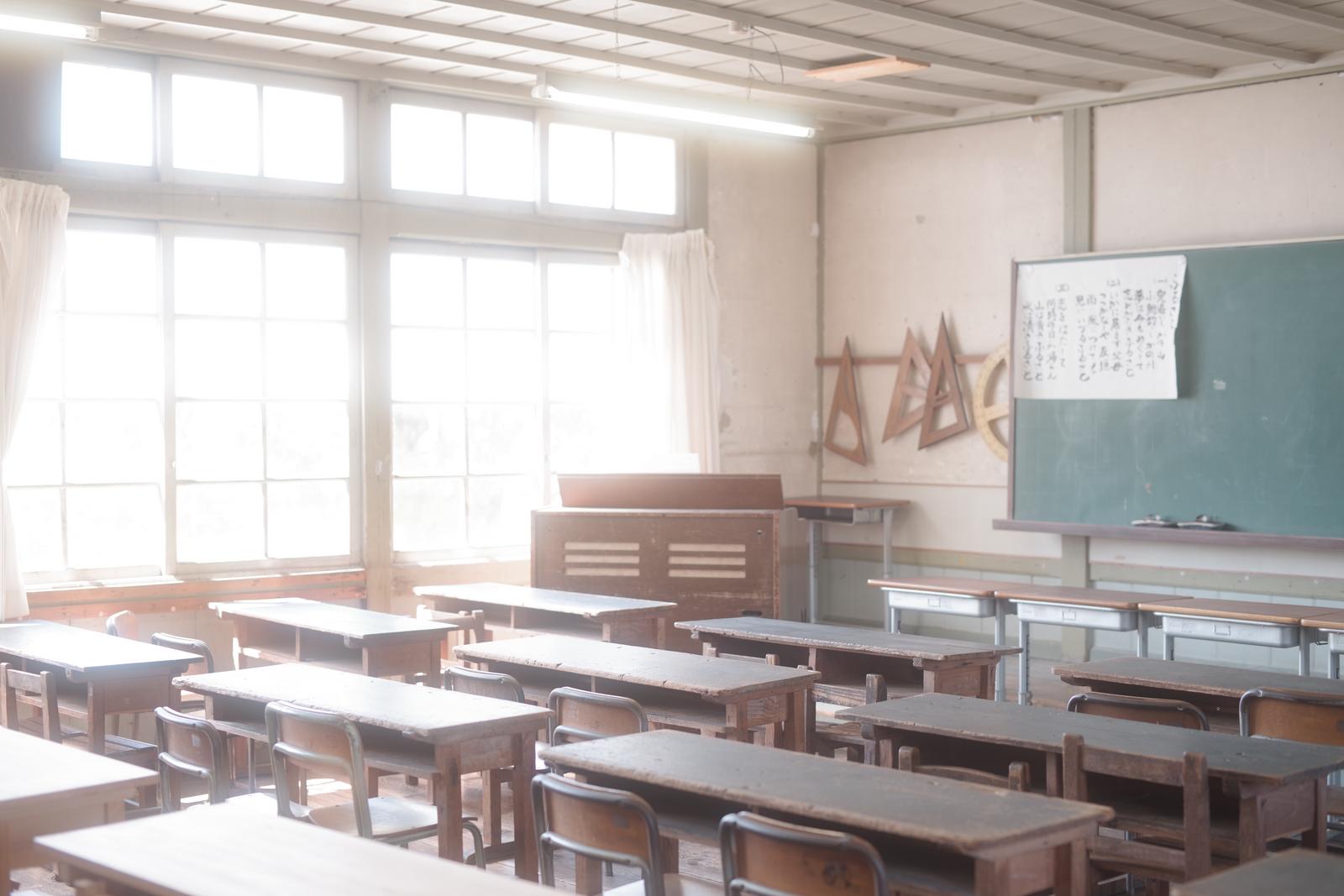 光が差し込む旧校舎の教室に並ぶ学習机と椅子