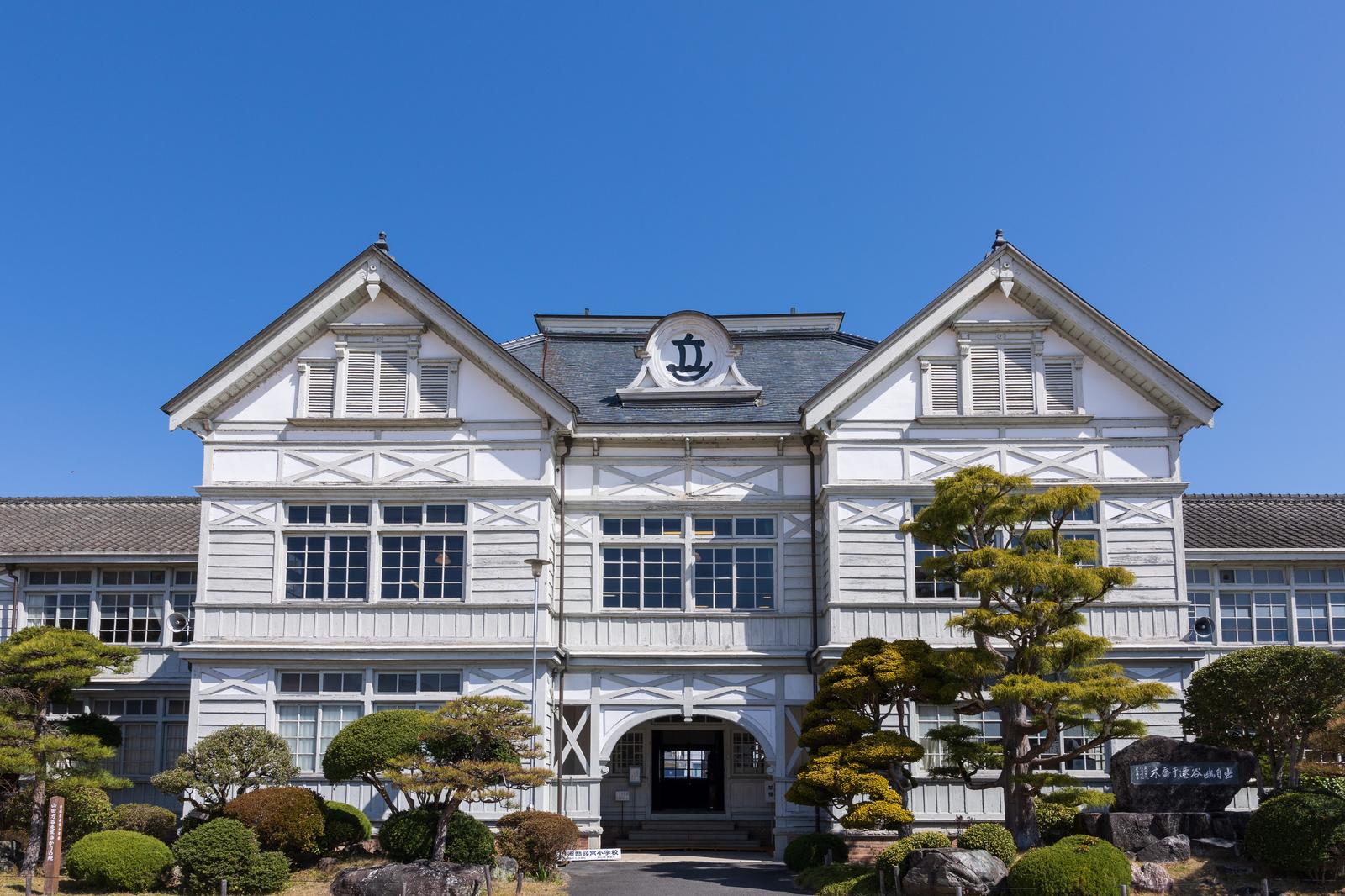 白い木造校舎の双塔屋根が青空に映える、旧遷喬尋常小学校の外観