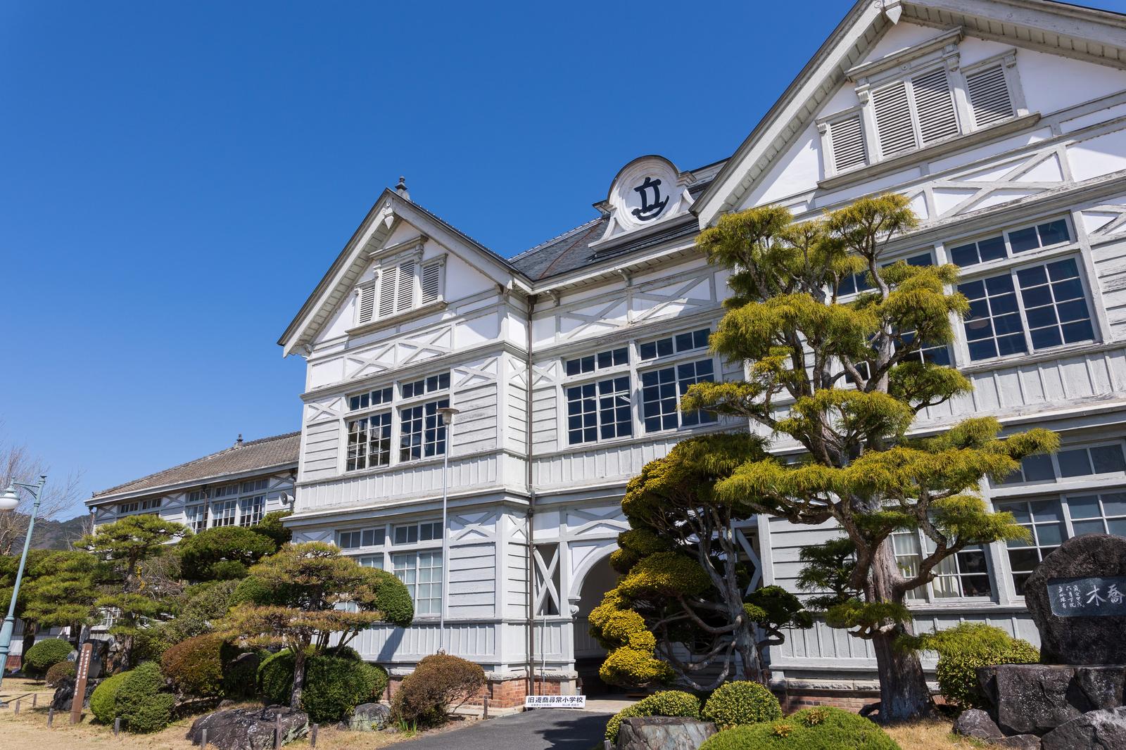 時計塔がある白い木造の洋館校舎と盆栽が植えられた庭園