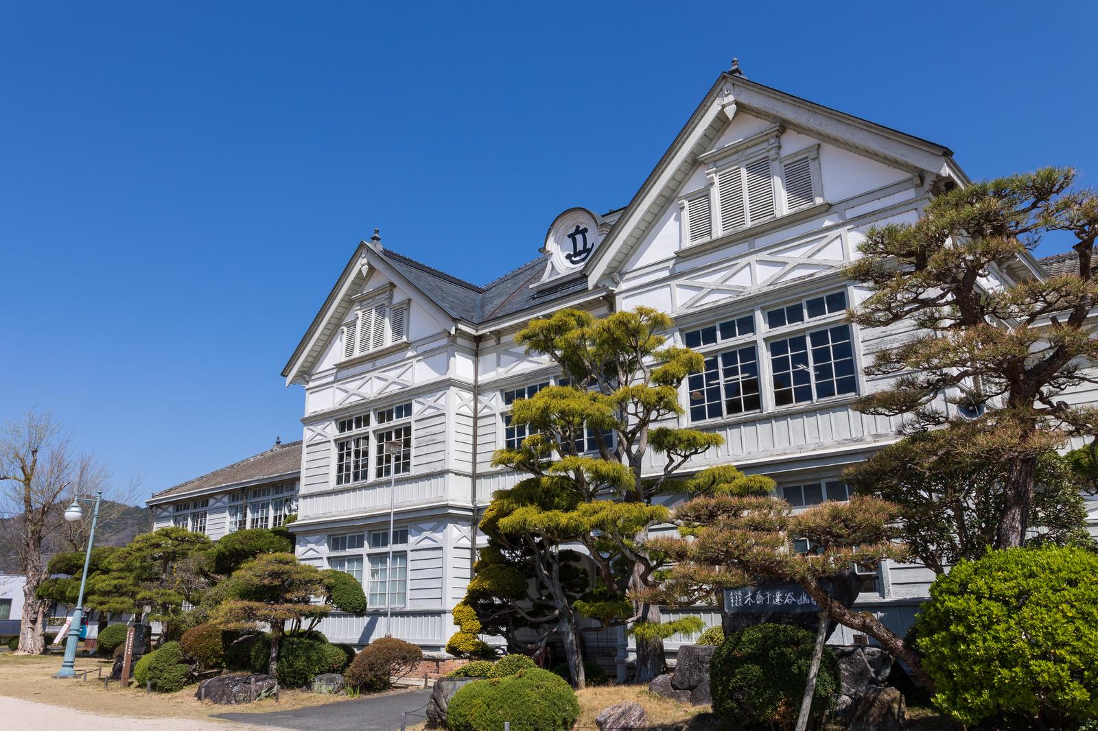 白い板張り壁とルネッサンス様式の屋根を持つ木造洋館校舎と盆栽松の庭園