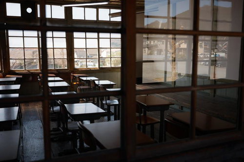 放課後の暗がりの教室で並ぶ学習机と椅子、窓からの光