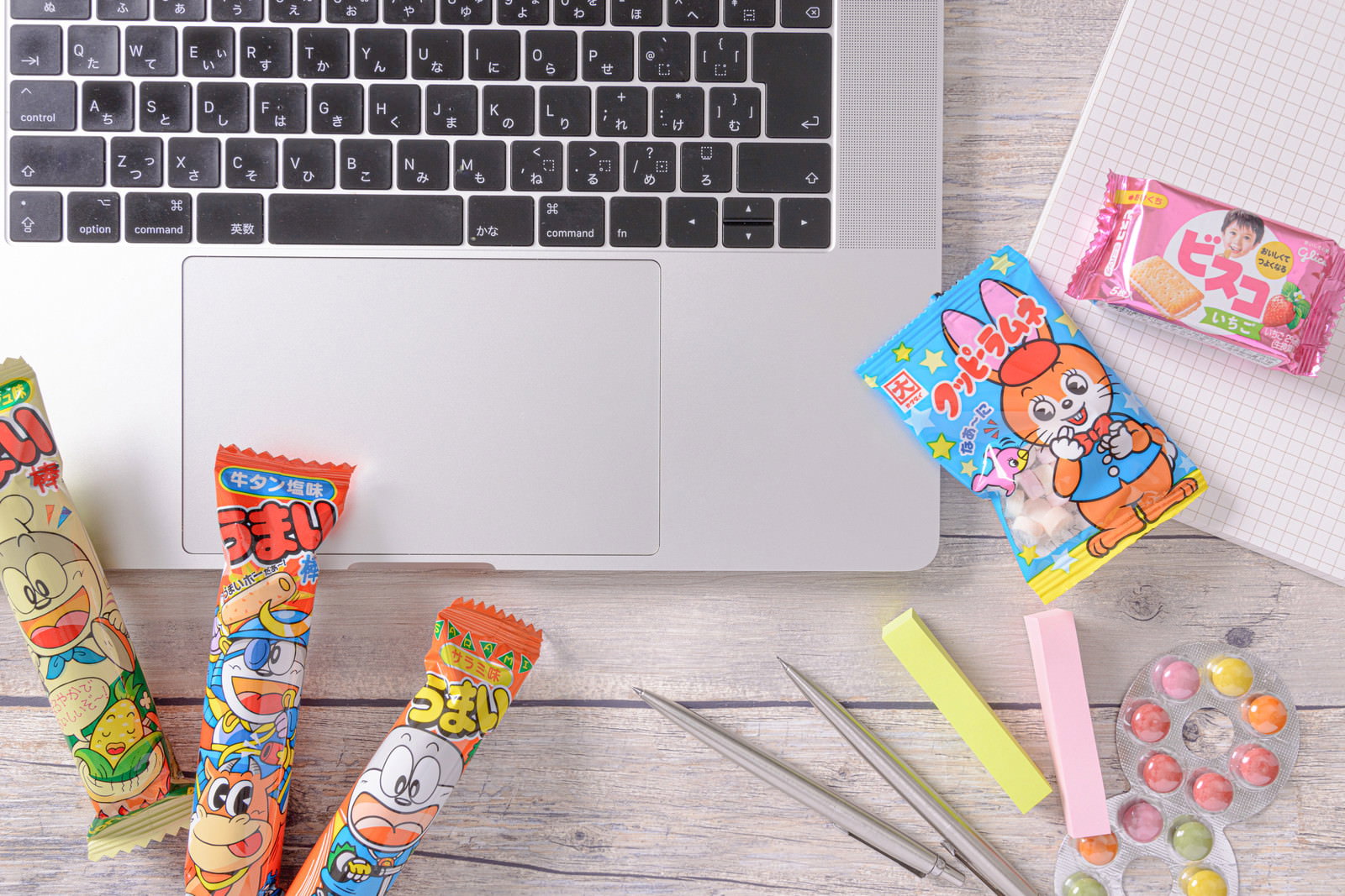 ノートパソコンのキーボードと一緒に配置されたうまい棒、ビスコ、ラムネなどのお菓子