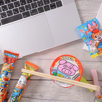 ブタメンやうまい棒に囲まれたノートパソコンのデスク風景の写真