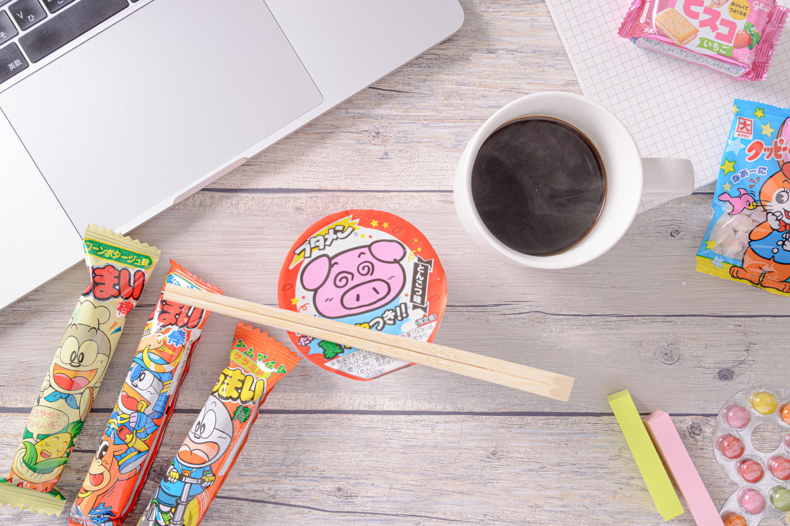 ノートパソコンとコーヒー、駄菓子が並ぶデスクの様子