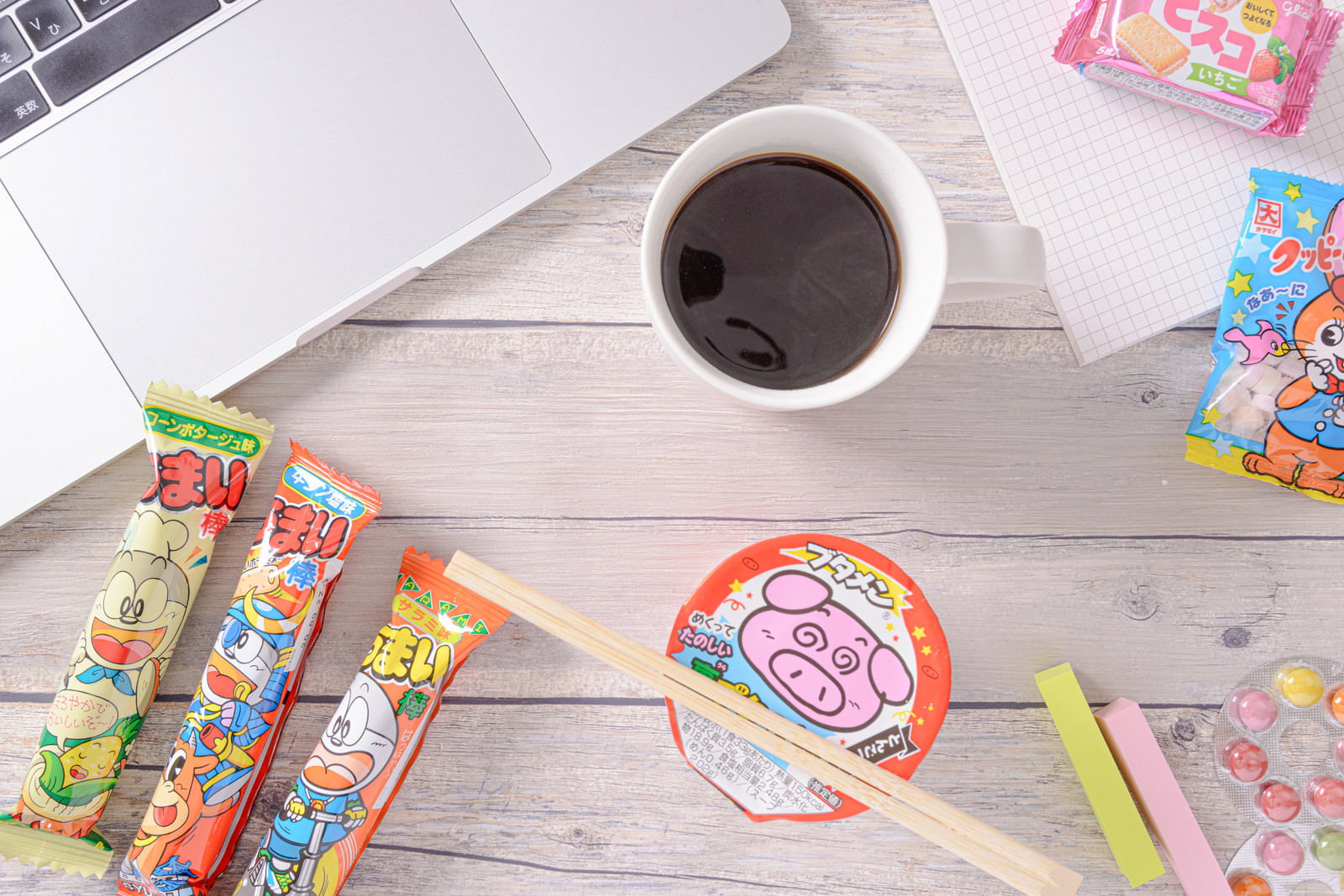 白い木目のテーブルに置かれたコーヒーカップとうまい棒やブタメンなどのお菓子