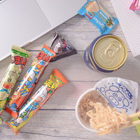 木製テーブルに散らばる食べかけのブタメンと缶ビール、お菓子の写真