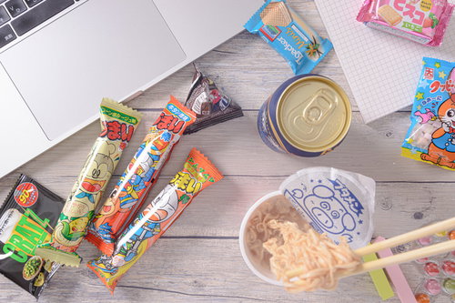 木製テーブルに散らばる食べかけのブタメンと缶ビール、お菓子