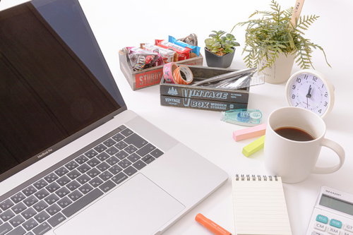 ノートパソコンの横に置かれたコーヒーとお菓子