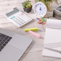 無造作に置かれた文具とノートパソコンのデスク風景の写真