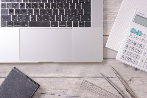 ノートPCと電卓を使った経理作業のデスクワーク