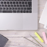 木目調のデスクに配置されたノート型パソコンとカラフルなクリップの写真