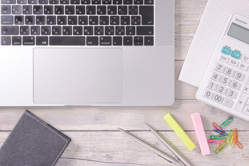 木目調のデスクに配置されたノート型パソコンとカラフルなクリップ