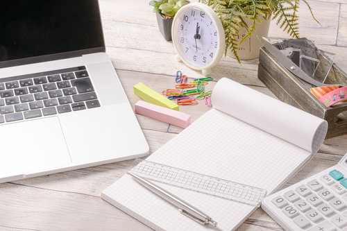白いデスクの上に散らばった文房具とノートパソコン