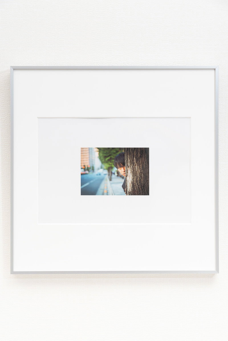 白い壁に掛けられた白いフレームの額縁に入った小さな写真［モデル：大川竜弥］