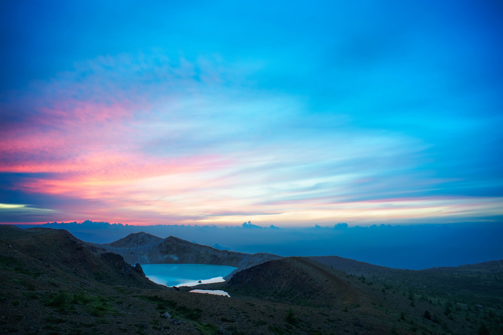 朝焼けの空の下、草津白根山の稜線と湯釜が美しく映える夜明けの風景