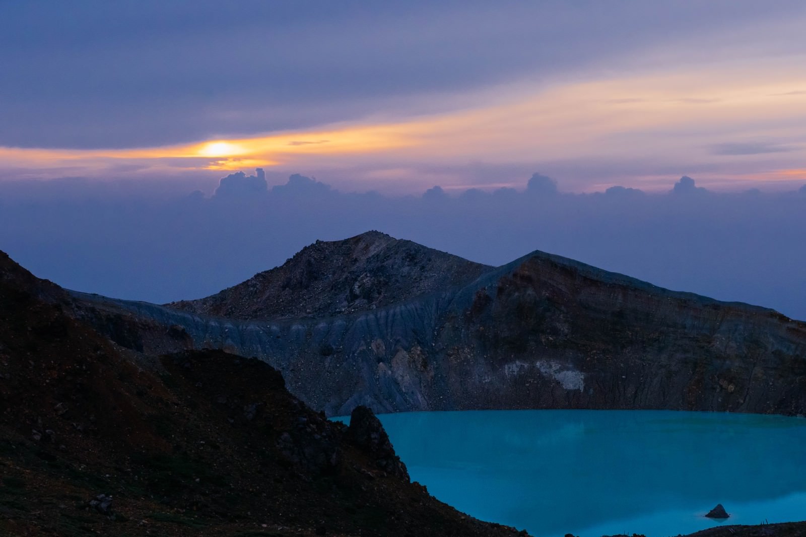 白根山の湯釜火口に朝日が射し込む夜明けの風景