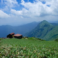 登山道に現れた赤い屋根の山小屋と連なる山峰の風景の写真